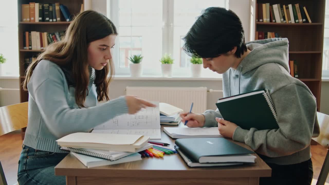 Studente a sinistra che apre gli appunti a spirale, mostrando evidenziazioni a linee sovrapposte, mentre il compagno a destra prende appunti di studio.