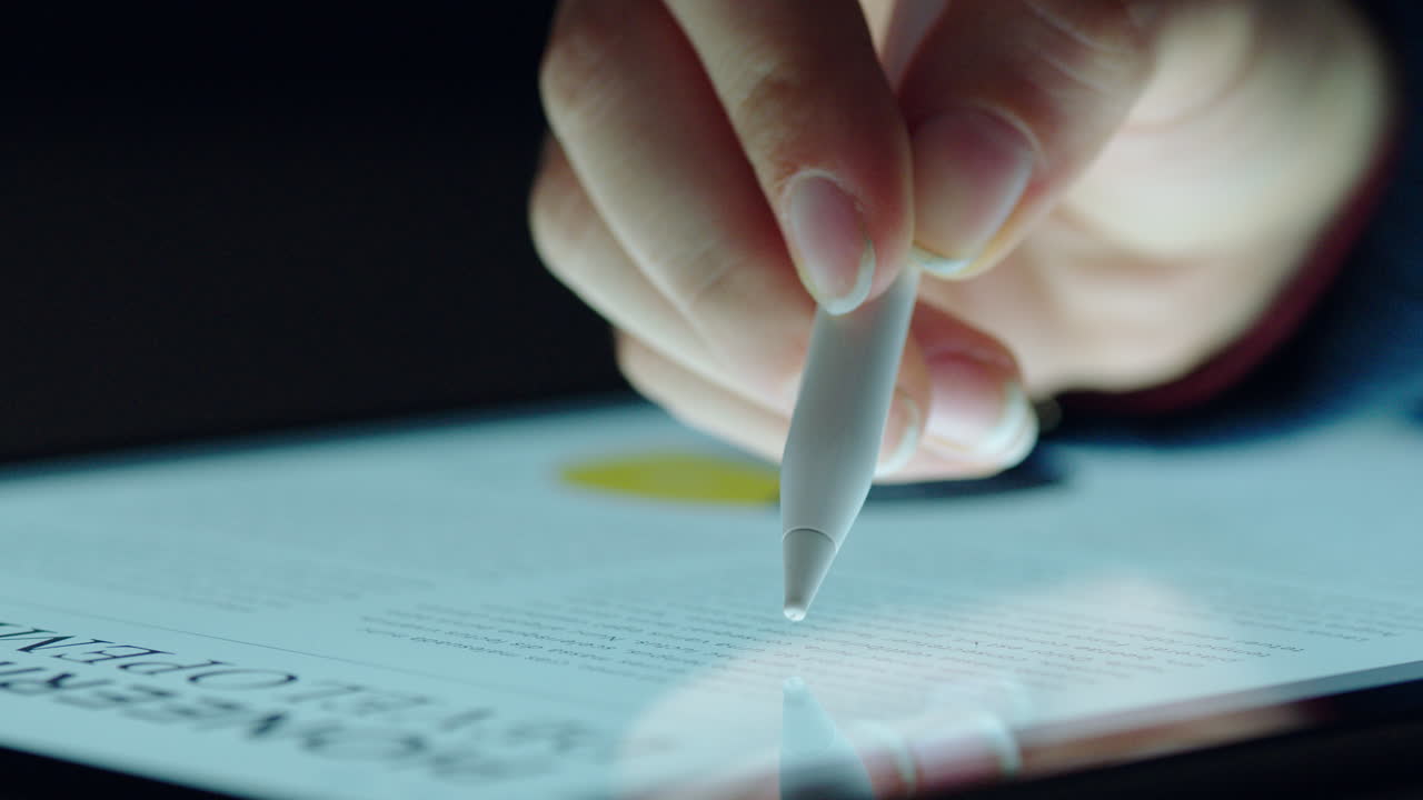 close up hand using stylus pen browsing digital tablet screen showing market graph statistics finance information on electronic touchscreen device