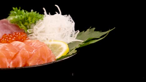 a platter of fresh sashimi including salmon, tuna, scallop, and salmon roe rotates smoothly against a black background under bright studio lighting