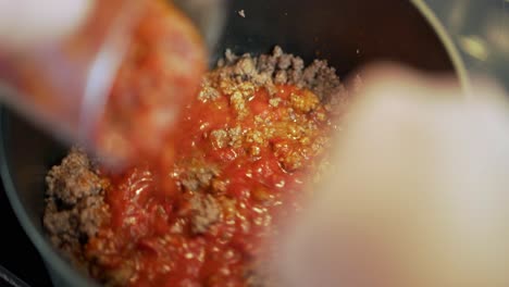 chile, tomato, bolognese sauce being added to ground or mince beef in black pot with some stirring