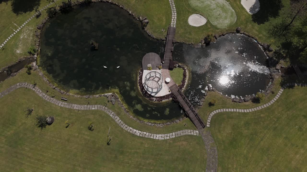 aerial shot of a gazebo on a small island with wooden bridges and tranquil surrounding pond