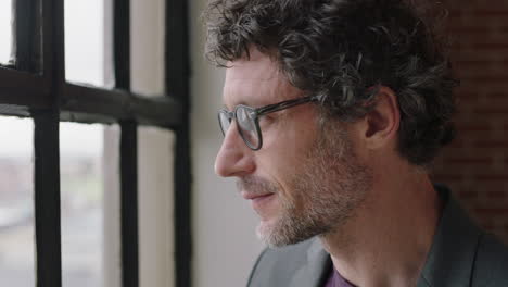 portrait-happy-mature-business-man-drinking-coffee-at-home-enjoying-relaxed-morning-looking-out-window-planning-ahead-thinking-successful-caucasian-male-smiling-wearing-glasses-in-apartment-loft