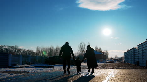 rear view of the couple with a little baby holding by hands walking outdoors. family of three heading to the car.