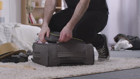 man struggling to pack full suitcase in bedroom at home for summer holiday 2