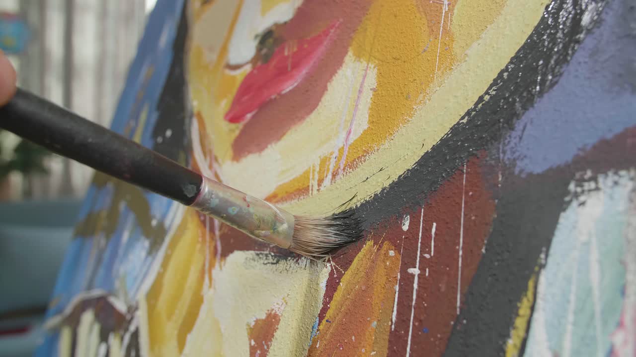 cerca de una mano sosteniendo un pincel de colores mixtos y pintando el rostro de una niña en el lienzo