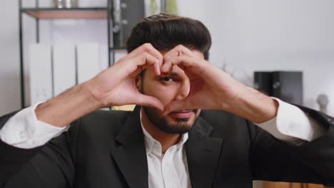 Indian-business-man-makes-symbol-of-love,-showing-heart-sign-to-camera,-express-romantic-feelings