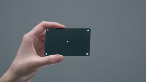 tarjeta de crédito o débito bancaria negra con puntos de seguimiento y espacio en blanco en mano femenina en fondo de estudio gris