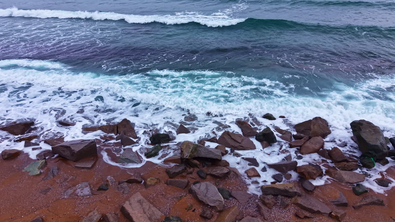 Onde si infrangono contro gli scogli su una spiaggia di giorno, vicino all'oceano, con cieli sereni e correnti leggere.