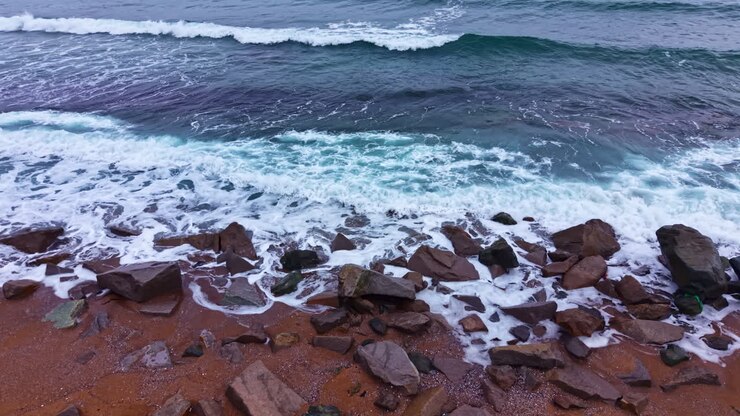 Onde si infrangono contro gli scogli su una spiaggia di giorno, vicino all'oceano, con cieli sereni e correnti leggere.