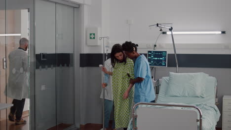 Afro-american-nurse-with-doctor-helping-patient-to-stand-up-from-bed