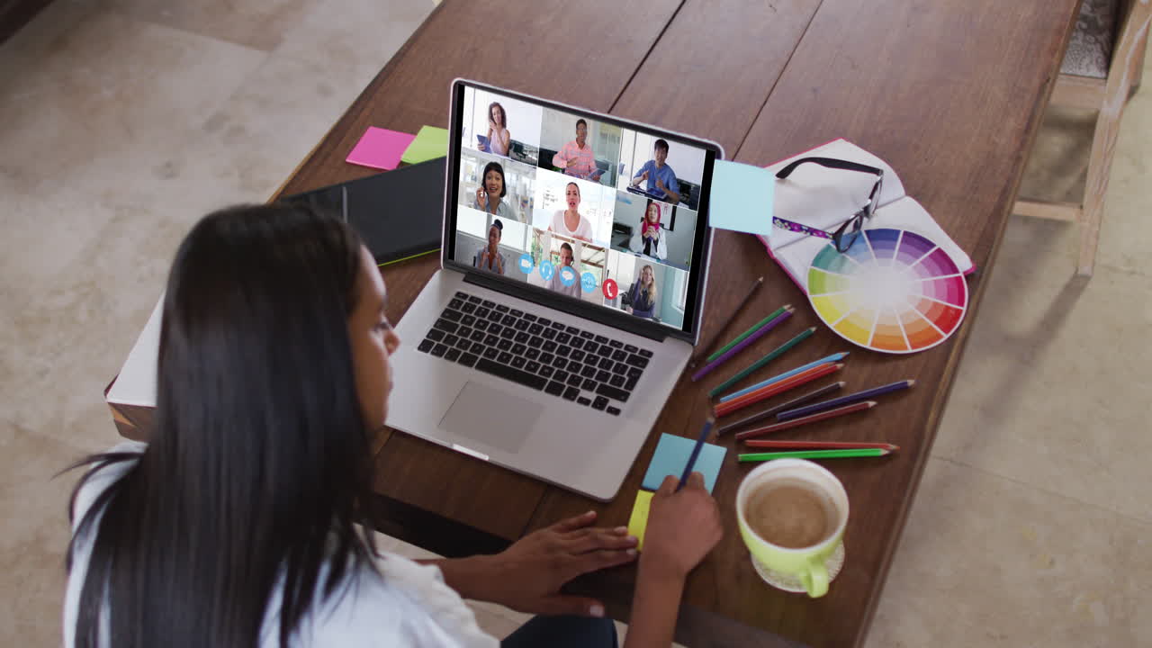 Mujer caucásica usando una laptop en videollamada con colegas, tomando notas