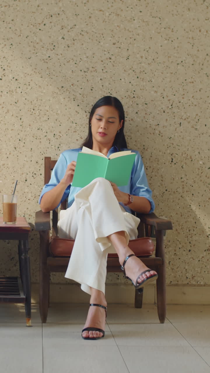Vertical of Asian Businesswoman Resting with Book and Coffee in Cafe