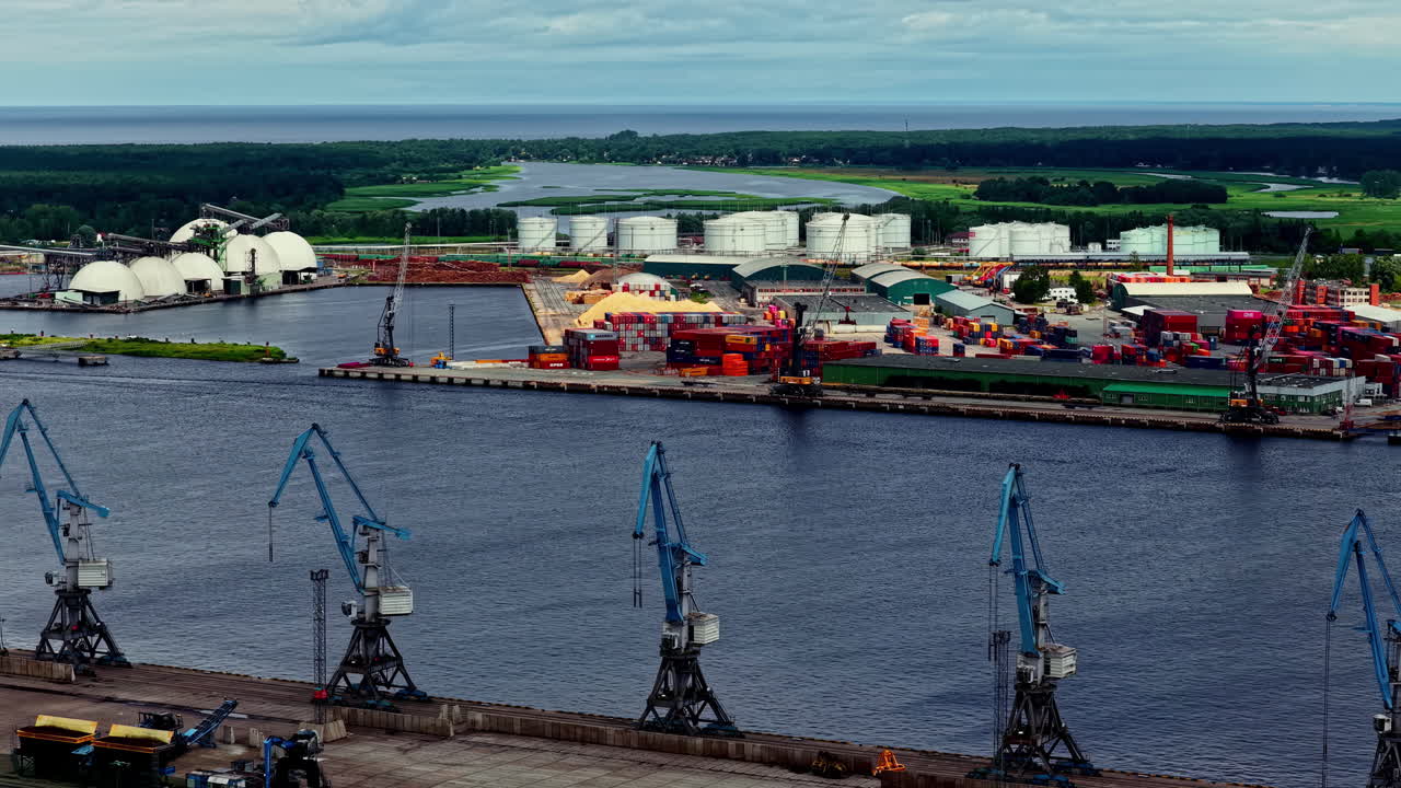 Diverse landscape of the Port of Riga, with harbor cranes in the foreground and various container, fertilizer, and oil terminals lining the Daugava River in Latvia