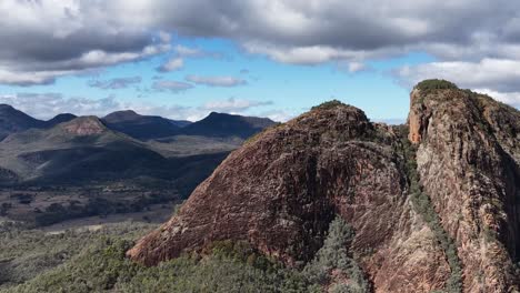 drone camera smoothly pans across split rock, revealing rugged cliffs, forested valleys, and distant mountain ranges under partly cloudy daylight skies