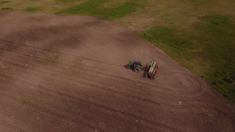 aerial shot of tractor plowing farm field with brown soil in agricultural area of argentina - wild birds flying over field and pecking seed