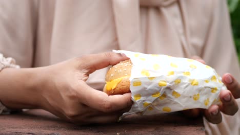 woman holding a cheeseburger in a paper wrapper