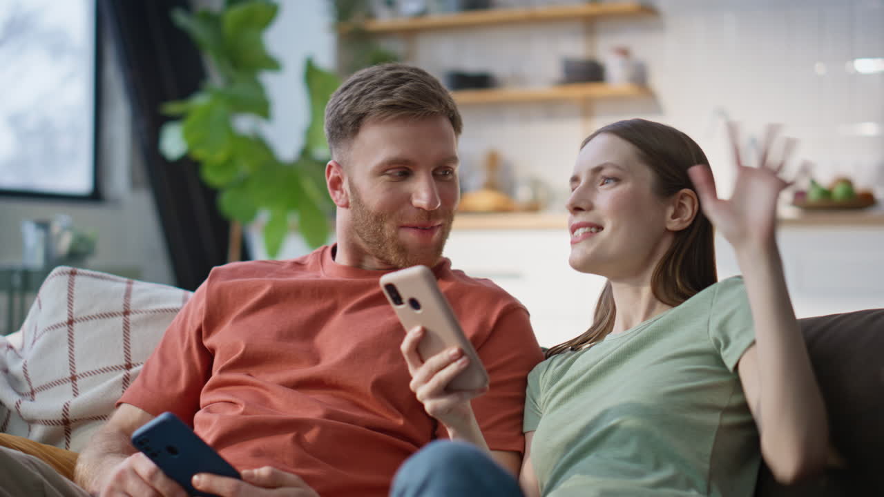 Talking couple holding smartphones sitting cozy couch living room closeup
