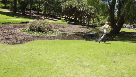 a woman jogs past a pond while the camera pans across with her