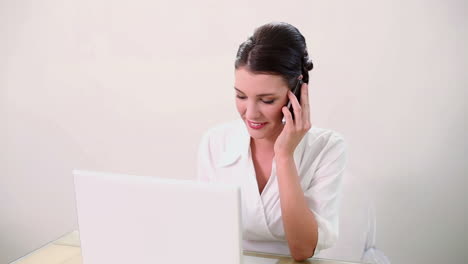 beautiful brunette using her laptop and talking on the phone