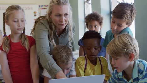 female teacher and group of kids using laptop in the class