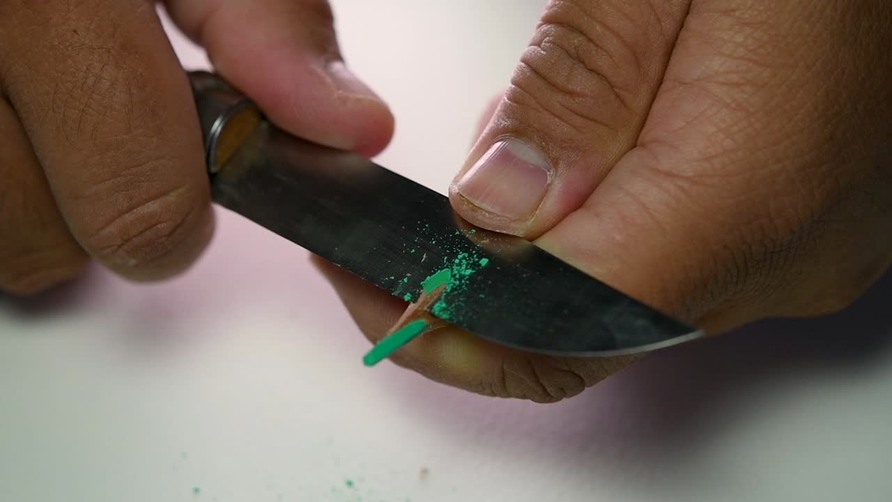 Footage of hands slowly sharpening a pencil and some coloured pencils with a sharp knife