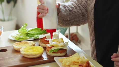 woman putting sauces on homemade burgers with lettuce, tomato and ham