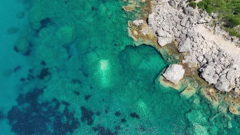 Aerial-shot-of-the-turquoise-waters-along-Corfu-Island,-Greece,-showcasing-the-rocky-coastline