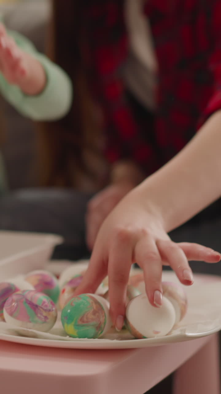 Happy sibling sisters prepare collection of bright eggs for Easter celebration at home slow motion. Ebru design and Christian holiday traditions