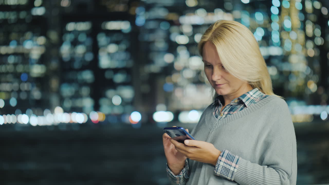 una mujer joven usa un teléfono inteligente en el fondo de las luces de la ciudad nocturna nueva york usa