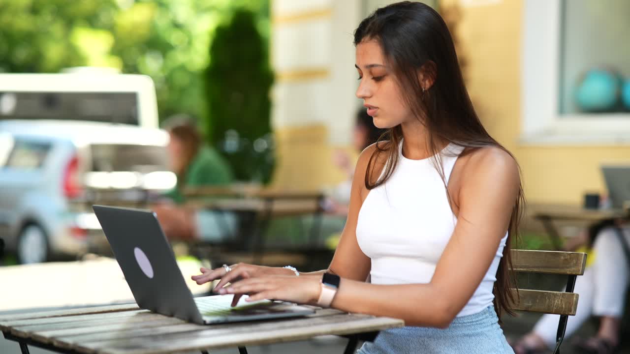 mujer joven trabajando en una computadora portátil en un café al aire libre