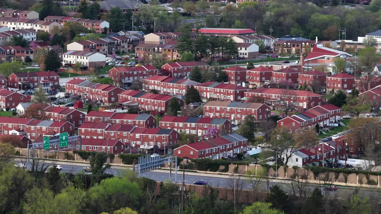 Dicht besiedeltes Viertel in Baltimore mit Reihen von roten Backstein-Reihenhäusern, nahegelegenem Straßenverkehr und städtischen Wohnstrukturen in einer typischen amerikanischen Ostküstenstadt-Kulisse. Weitwinkel-Luftaufnahme. Vielbefahrene Autobahnstraße.