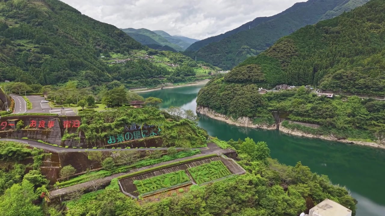 Cảnh quay drone bay qua khúc quanh sông hồ chứa xanh biếc với chữ cái tiếng Nhật được khắc trên sườn đồi núi bậc thang