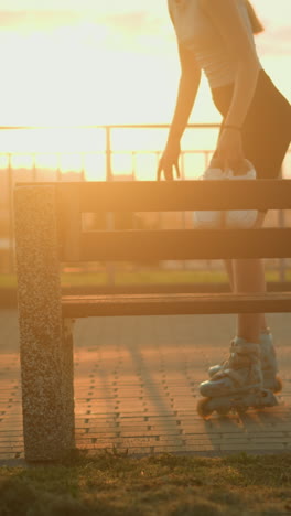 joven patinando hacia un banco al aire libre con zapatillas blancas en la mano durante la puesta de sol de la noche, la luz del sol crea un brillo cálido con largas sombras en el pavimento