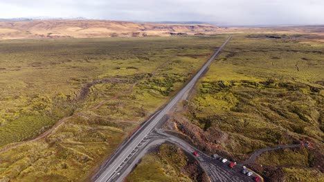 Eine-Einsame-Straße-Schlängelt-Sich-Durch-Isländische-Mooslandschaft,-Fahrzeuge-In-Bewegung,-Luftaufnahme