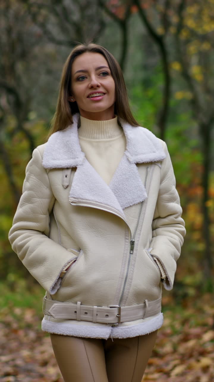 Happy Caucasian lady with long dark hair posing in front of camera in the park. Woman turns smiling to the camera. Autumn nature backdrop.