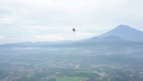 印尼傳統氣球的空中追蹤拍攝,旗<unk>在鄉村山地風景中的雲之間飛翔