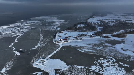 Vista-Panorámica-De-La-Estación-De-Anillamiento-De-Aves-En-El-Cabo-Vente-Y-El-Muelle-Que-Conduce-A-La-Laguna-De-Curlandia-En-Invierno,-Cuando-Todo-Está-Congelado-Y-Cubierto-De-Nieve.