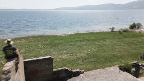 ruina con un tipo en él al lado de un gran lago con montañas en el fondo