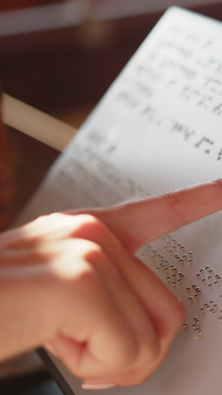 Il dito di una persona che traccia il Braille su una pagina, evidenziando il processo di lettura tattile, video verticale.