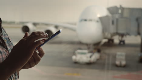 Woman's-Hands-With-A-Smartphone-Writes-A-Message-On-The-Background-Of-The-Airliner-Outside-The-Airpo