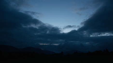 sunset above scottish mountains, slow moving dark blue clouds, dark silhouetted mountain landscape, dusk in countryside