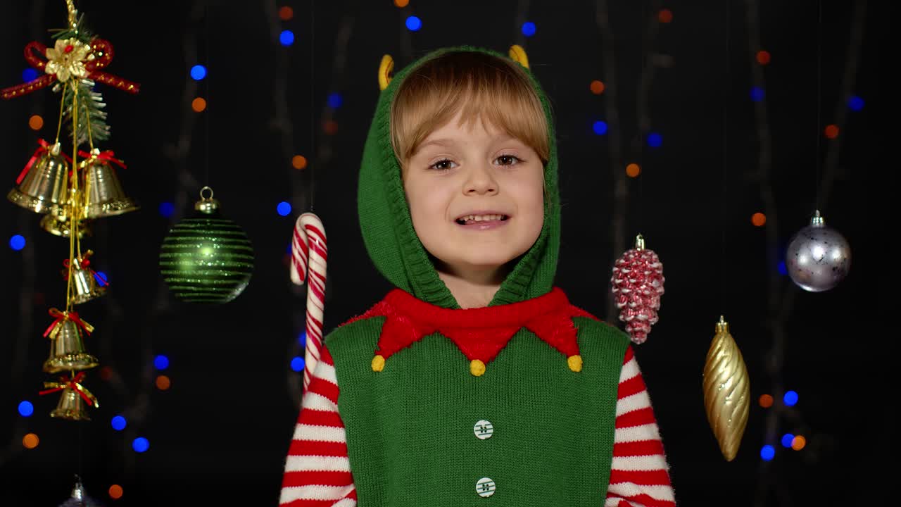 Dívka v kostýmu vánočního skřítka, pomocníka Santy, mává na pozdrav rukou. Ahoj, nazdar, gesto pozdravu.