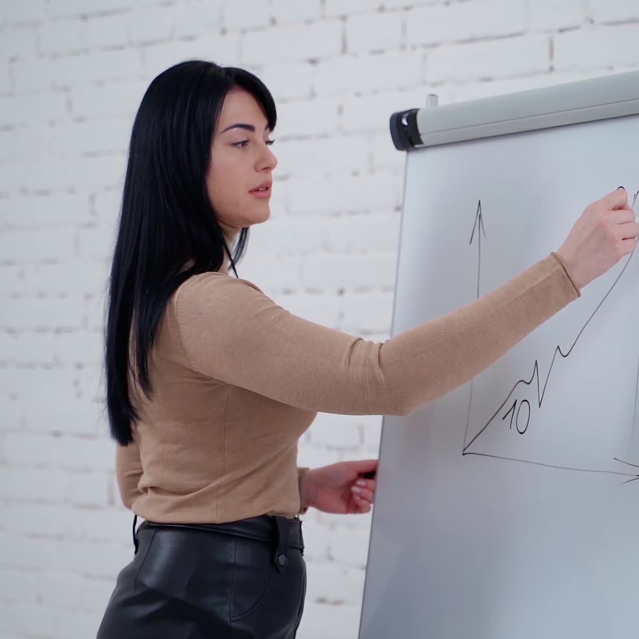 Female freelancer writing on a board. Beautiful young woman is writing graphics on a white board in the light room.