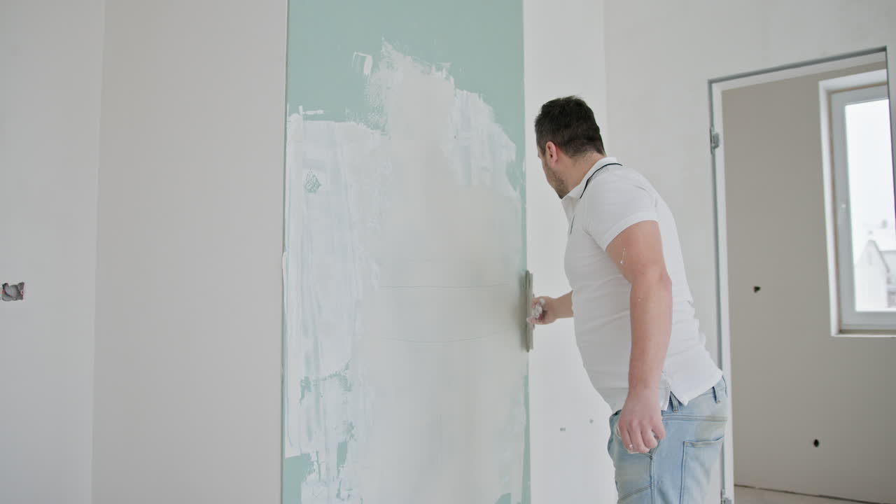 hombre enyesando una pared en una habitación en renovación.