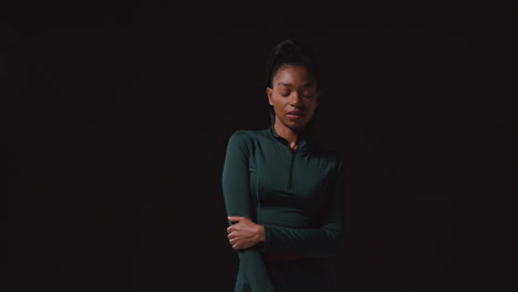 Portrait-Of-Determined-Female-Athlete-Wearing-Tracksuit-Training-Warming-Up-And-Stretching-Against-Black-Studio-Background-1