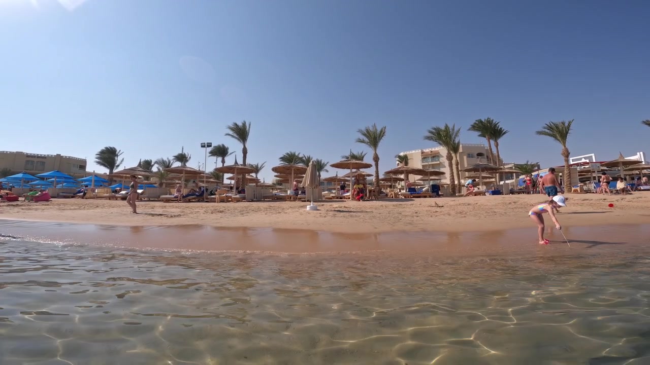 Immagine di onde che si infrangono verso una spiaggia di sabbia bianca con turisti che si godono la spiaggia in una luminosa giornata di sole