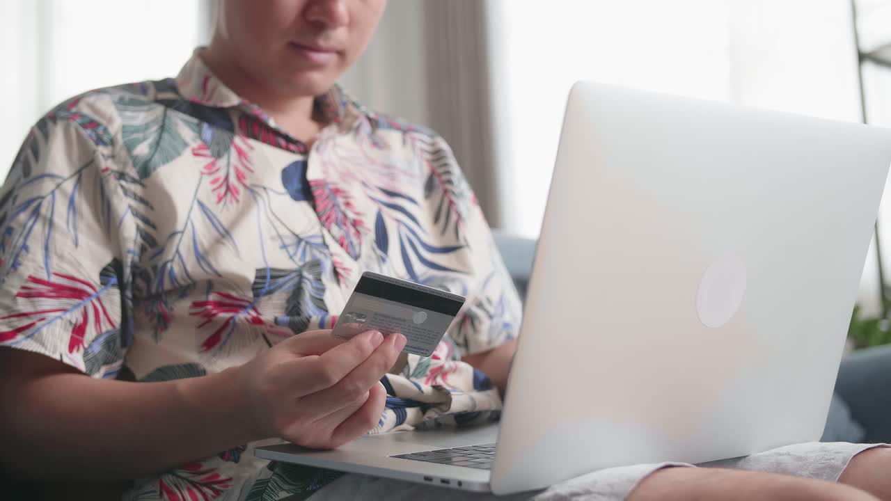 Primo piano di una mano che tiene una carta di credito e usa un computer portatile per fare acquisti online in salotto.
