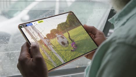 video of person sitting on the couch and watching football match on tablet