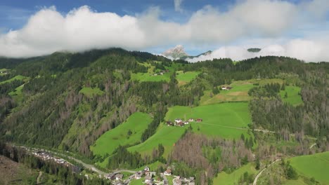 drone flies fast forwards above chalets and alpine houses that dot the lush green grass hills