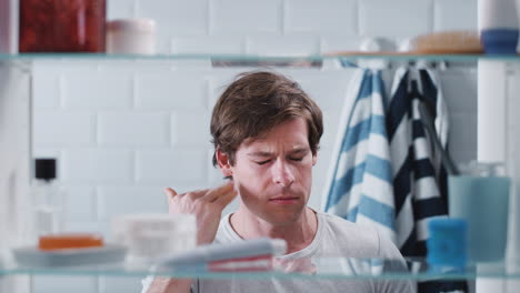 view through bathroom cabinet of man brushing teeth before going to work